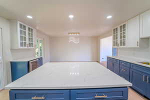 Kitchen featuring blue cabinetry, a center island, white cabinets, and beverage cooler