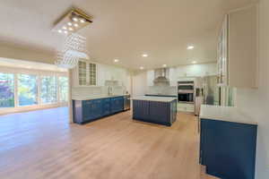 Kitchen featuring wall chimney range hood, sink, appliances with stainless steel finishes, a center island, and white cabinets