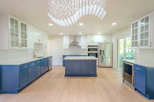 Kitchen with wall chimney range hood, white cabinetry, beverage cooler, appliances with stainless steel finishes, and light hardwood / wood-style floors