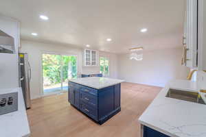 Kitchen with white cabinets, blue cabinets, stainless steel refrigerator, light hardwood / wood-style floors, and a center island