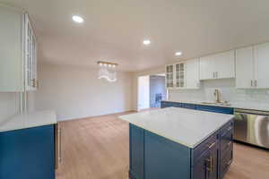 Kitchen with sink, dishwasher, a kitchen island, white cabinetry, and light hardwood / wood-style floors