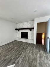 Unfurnished living room featuring a stone fireplace, a textured ceiling, and dark wood-type flooring