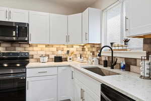 Kitchen with white cabinetry, black appliances, sink, and decorative backsplash