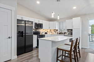 Kitchen featuring appliances with stainless steel finishes, a center island, white cabinetry, lofted ceiling, and pendant lighting