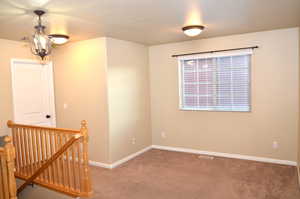 Carpeted empty room featuring a notable chandelier