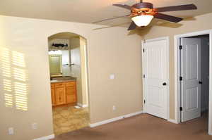 Unfurnished bedroom featuring light carpet, ensuite bath, and ceiling fan