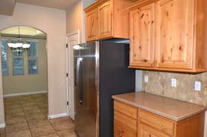 Kitchen with backsplash, stainless steel fridge, light tile patterned flooring, and a chandelier