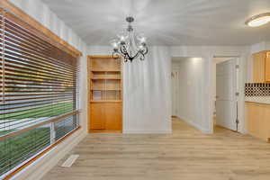 Unfurnished dining area featuring an inviting chandelier and light wood-type flooring