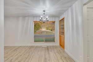 Unfurnished room featuring an inviting chandelier and light wood-type flooring