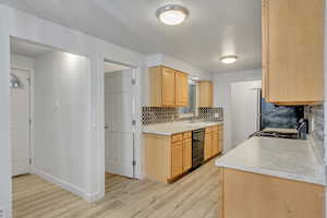 Kitchen with backsplash, black appliances, sink, light brown cabinetry, and light hardwood / wood-style floors