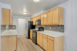 Kitchen featuring black appliances, sink, light hardwood / wood-style floors, decorative backsplash, and light brown cabinets