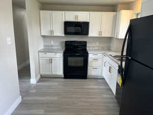 Kitchen featuring white cabinets, baseboards, light countertops, and black appliances