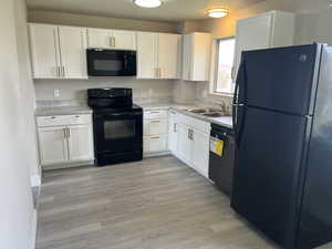 Kitchen featuring light wood-type flooring, white cabinetry, black appliances, light countertops, and a sink