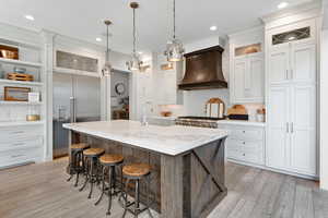 Kitchen featuring a center island with sink, decorative backsplash, premium range hood, and stainless steel appliances