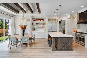 Kitchen with tasteful backsplash, an island with sink, white cabinetry, high quality appliances, and decorative light fixtures