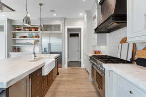 Kitchen featuring sink, decorative light fixtures, custom exhaust hood, appliances with stainless steel finishes, and light hardwood / wood-style floors