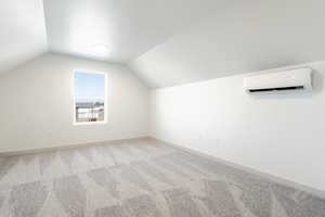 Bonus room featuring light carpet, vaulted ceiling, and an AC wall unit