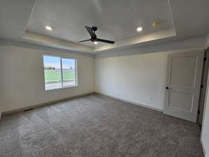 Empty room featuring ceiling fan, carpet, and a tray ceiling