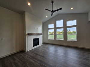 Unfurnished living room with ceiling fan, a textured ceiling, high vaulted ceiling, dark wood-type flooring, and a fireplace