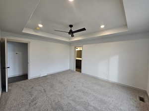 Unfurnished bedroom featuring ceiling fan, carpet flooring, and a tray ceiling