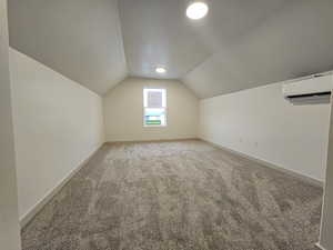 Additional living space with an AC wall unit, a textured ceiling, vaulted ceiling, and carpet floors