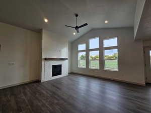 Unfurnished living room featuring dark hardwood / wood-style floors, a tile fireplace, a textured ceiling, high vaulted ceiling, and ceiling fan