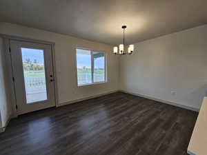 Unfurnished dining area with an inviting chandelier, a textured ceiling, a water view, and dark hardwood / wood-style flooring