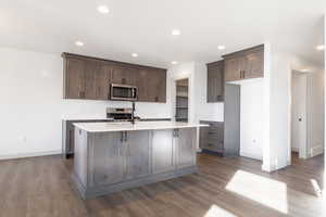 Kitchen with dark hardwood / wood-style flooring, tasteful backsplash, dark brown cabinets, stainless steel appliances, and a center island with sink