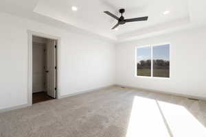 Carpeted spare room featuring a tray ceiling and ceiling fan