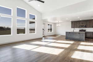 Unfurnished living room featuring wood-type flooring, ceiling fan with notable chandelier, high vaulted ceiling, and sink