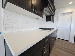 Kitchen with dark brown cabinets, stainless steel gas stovetop, dark hardwood / wood-style floors, and backsplash