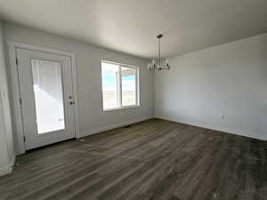 Unfurnished dining area with dark wood-type flooring and a chandelier