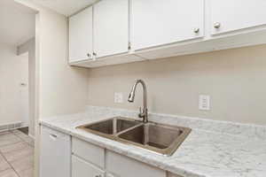 Kitchen with white cabinetry, light tile patterned flooring, sink, and dishwasher