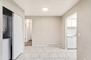 Laundry area with stacked washer and dryer and light tile patterned floors