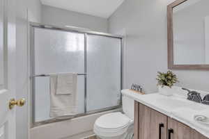 Full bathroom featuring vanity, enclosed tub / shower combo, and toilet