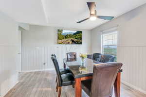 Dining space with ceiling fan, wood walls, and light hardwood / wood-style flooring