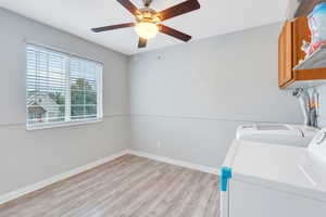 Washroom with cabinets, light hardwood / wood-style flooring, separate washer and dryer, and ceiling fan