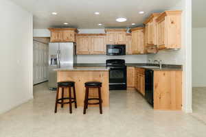 Kitchen with black appliances, recessed lighting, light brown cabinetry, a sink, and a breakfast bar