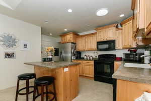 Kitchen featuring light brown cabinets, sink, black appliances, a center island, and a kitchen bar