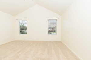 Spare room featuring light colored carpet, high vaulted ceiling, and baseboards
