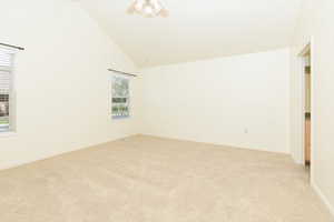 Empty room featuring light carpet, a ceiling fan, baseboards, and high vaulted ceiling
