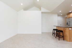 Kitchen with stainless steel refrigerator with ice dispenser, a breakfast bar area, dark countertops, recessed lighting, and vaulted ceiling