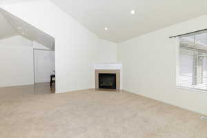Unfurnished living room featuring lofted ceiling, light colored carpet, recessed lighting, a fireplace with flush hearth, and baseboards