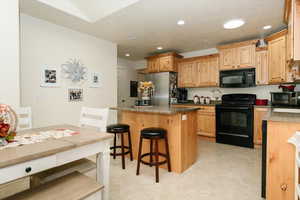 Kitchen with a breakfast bar, black appliances, light brown cabinetry, and a kitchen island