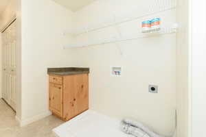 Laundry area featuring hookup for an electric dryer, hookup for a washing machine, light tile patterned floors, and baseboards