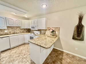 Kitchen featuring a peninsula, tasteful backsplash, a sink, and white appliances