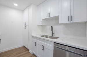 Kitchen with stainless steel dishwasher, sink, white cabinetry with pantry, and light hardwood / wood-style floors