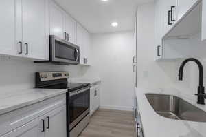 Kitchen featuring appliances with stainless steel finishes, sink, white cabinetry, light stone counters, and light hardwood / wood-style flooring