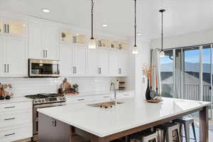 Kitchen featuring an island with sink, backsplash, sink, pendant lighting, and appliances with stainless steel finishes