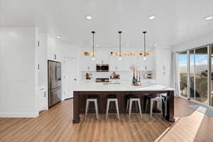 Kitchen with a center island with sink, a breakfast bar, pendant lighting, light  wood-style floors, and stainless steel appliances